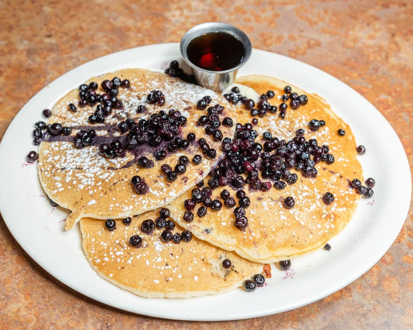 Fluffy blueberry pancakes dusted with powdered sugar, served with a side of maple syrup.