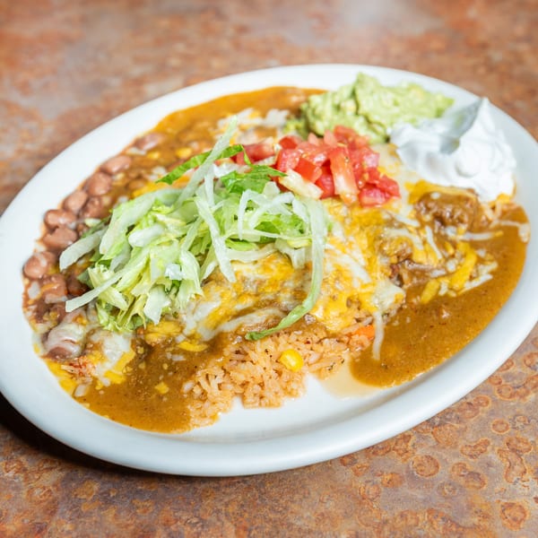 Mexican combo plate with cheesy enchiladas, rice, beans, lettuce, tomatoes, guacamole, and sour cream.