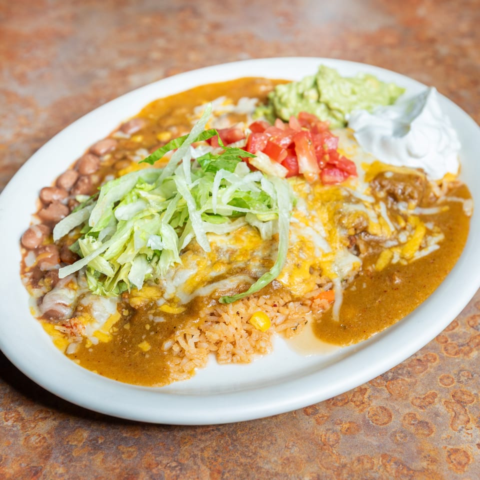 Mexican combo plate with cheesy enchiladas, rice, beans, lettuce, tomatoes, guacamole, and sour cream.