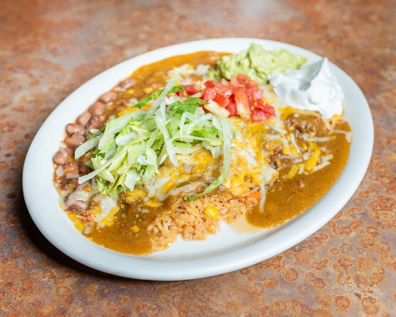 Mexican combo plate with cheesy enchiladas, rice, beans, lettuce, tomatoes, guacamole, and sour cream.