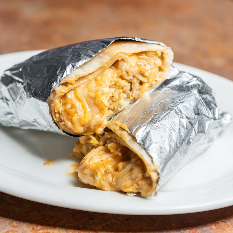 Cheesy burrito cut in half, wrapped in foil, served on a white plate.