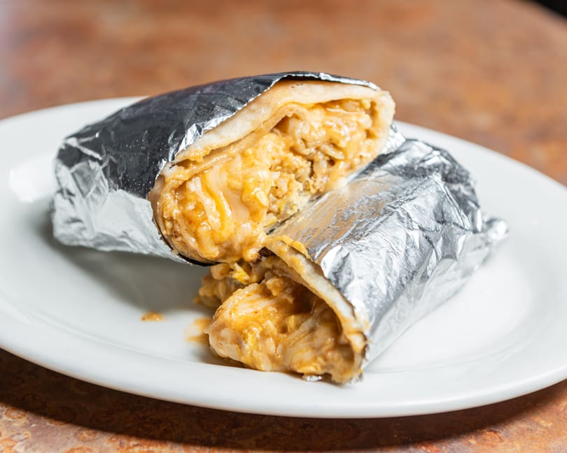 Cheesy burrito cut in half, wrapped in foil, served on a white plate.