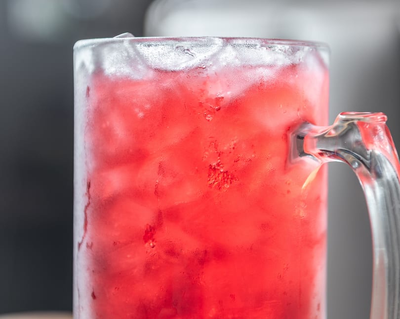 Frosty mug filled with a vibrant red drink and ice, covered in condensation.