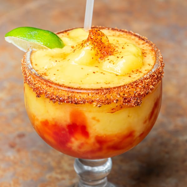 Frozen mango drink with red swirls, chili-lime rim, and a fresh lime wedge.