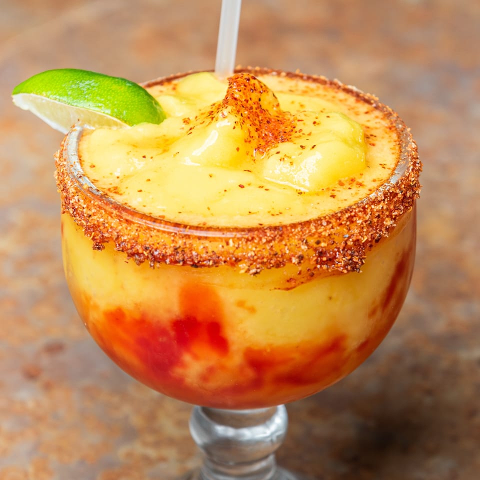Frozen mango drink with red swirls, chili-lime rim, and a fresh lime wedge.