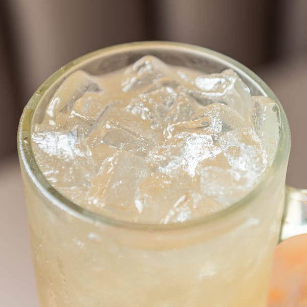 Glass mug filled with ice cubes and a light yellow drink, showing condensation.