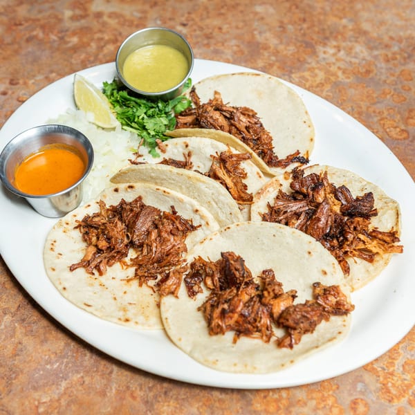 Plate of six shredded meat tacos with two sauces, lime, cilantro, and diced onions.