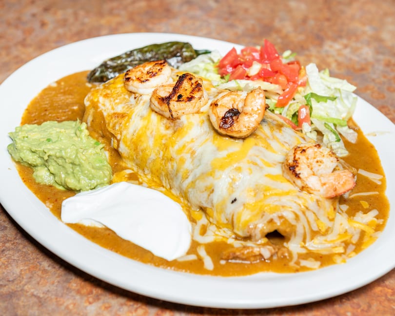 Cheesy shrimp burrito with grilled shrimp, guacamole, sour cream, side salad, and green chili.