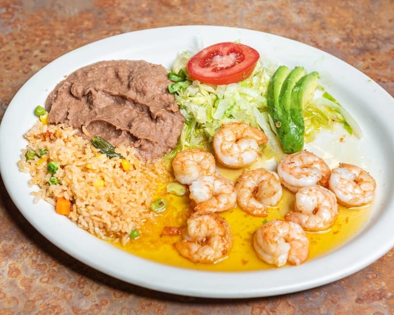 Delicious shrimp dish with rice, refried beans, lettuce, tomato, and avocado slices.